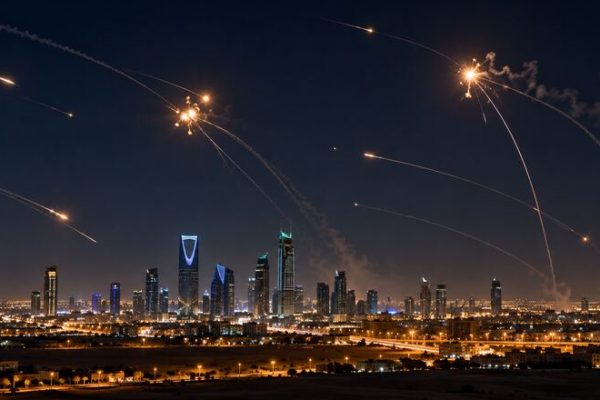 Silueta urbana saudí bajo un cielo nocturno con defensas aéreas interceptando proyectiles.